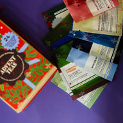A box of Advent Tea alongside a fan of individual tea sachets in various holiday colors, arranged on a solid purple background.