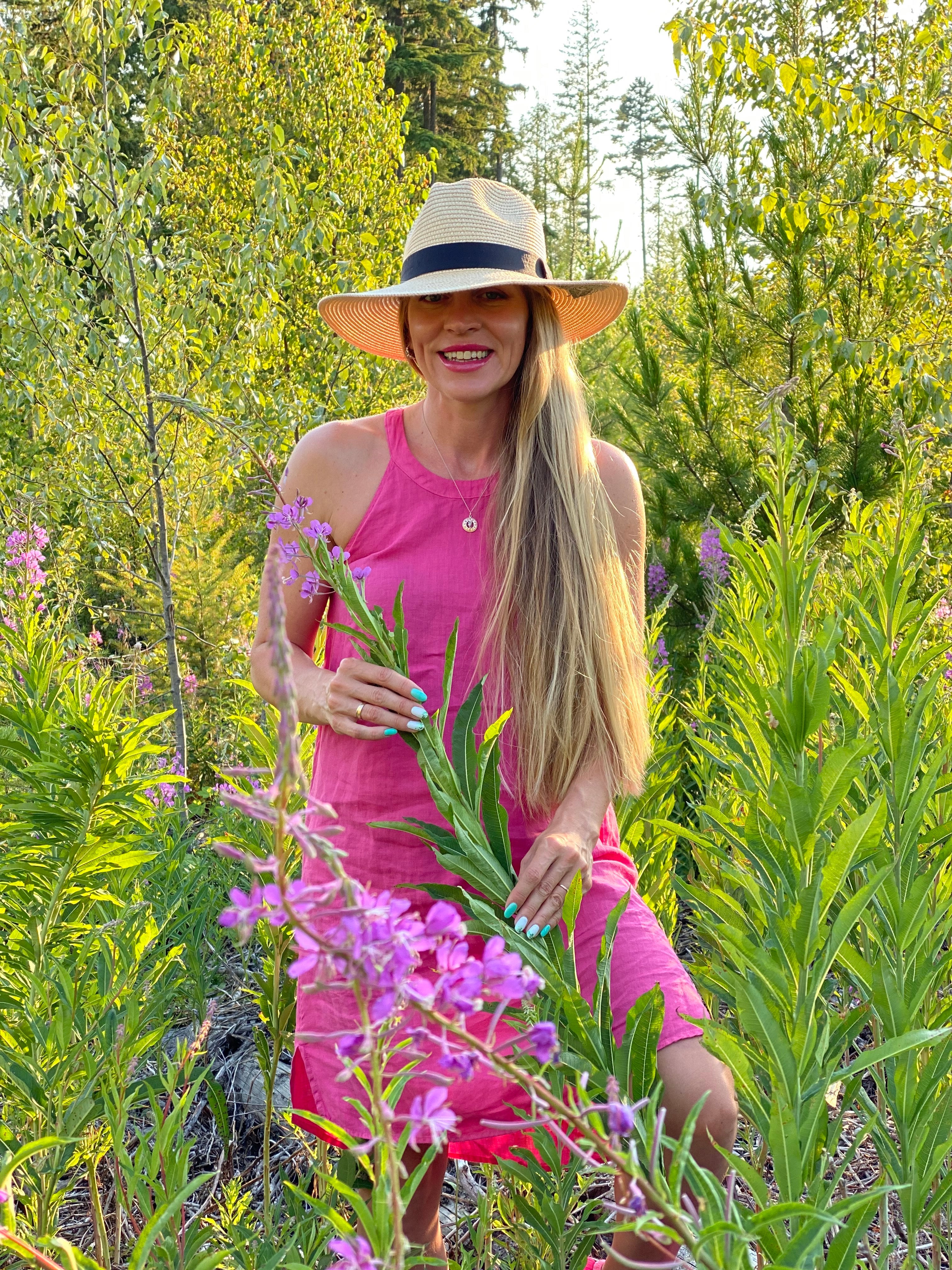 Smiling woman in pink dress and wide hat among pink wildflowers.
