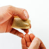 A close-up of a person's hands holding a small beige fabric pouch and pulling a thin white thread through it, against a plain white background.