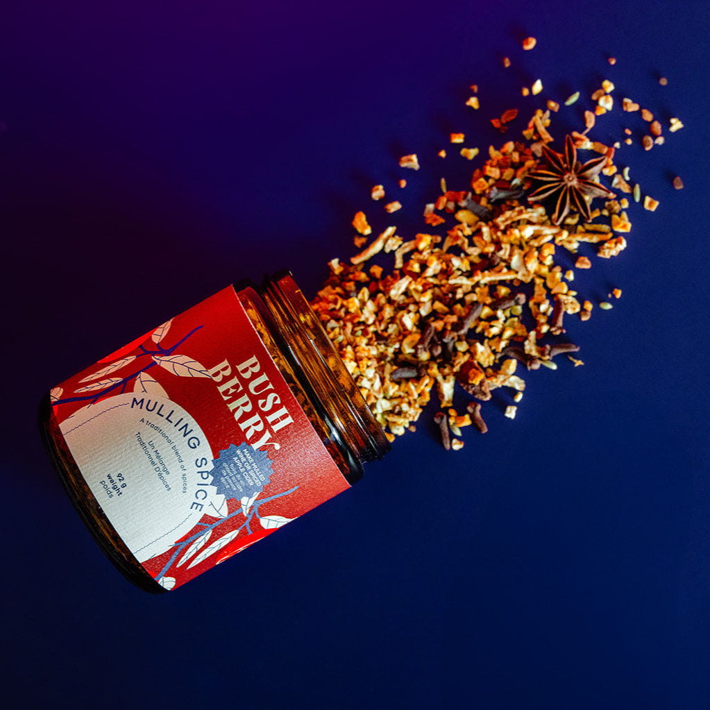Bottle of Bush Berry's Mulling Spice with spices spilling out on a dark blue background
