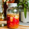 Glass jar with a metal lid containing a colorful drink on a wooden surface with a blurred background