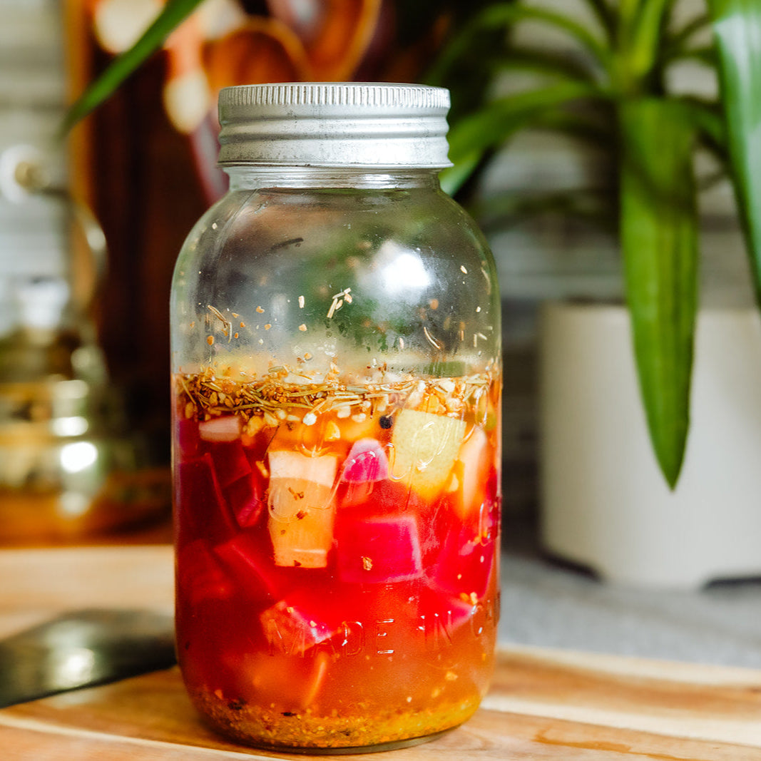 Glass jar with a metal lid containing a colorful drink on a wooden surface with a blurred background