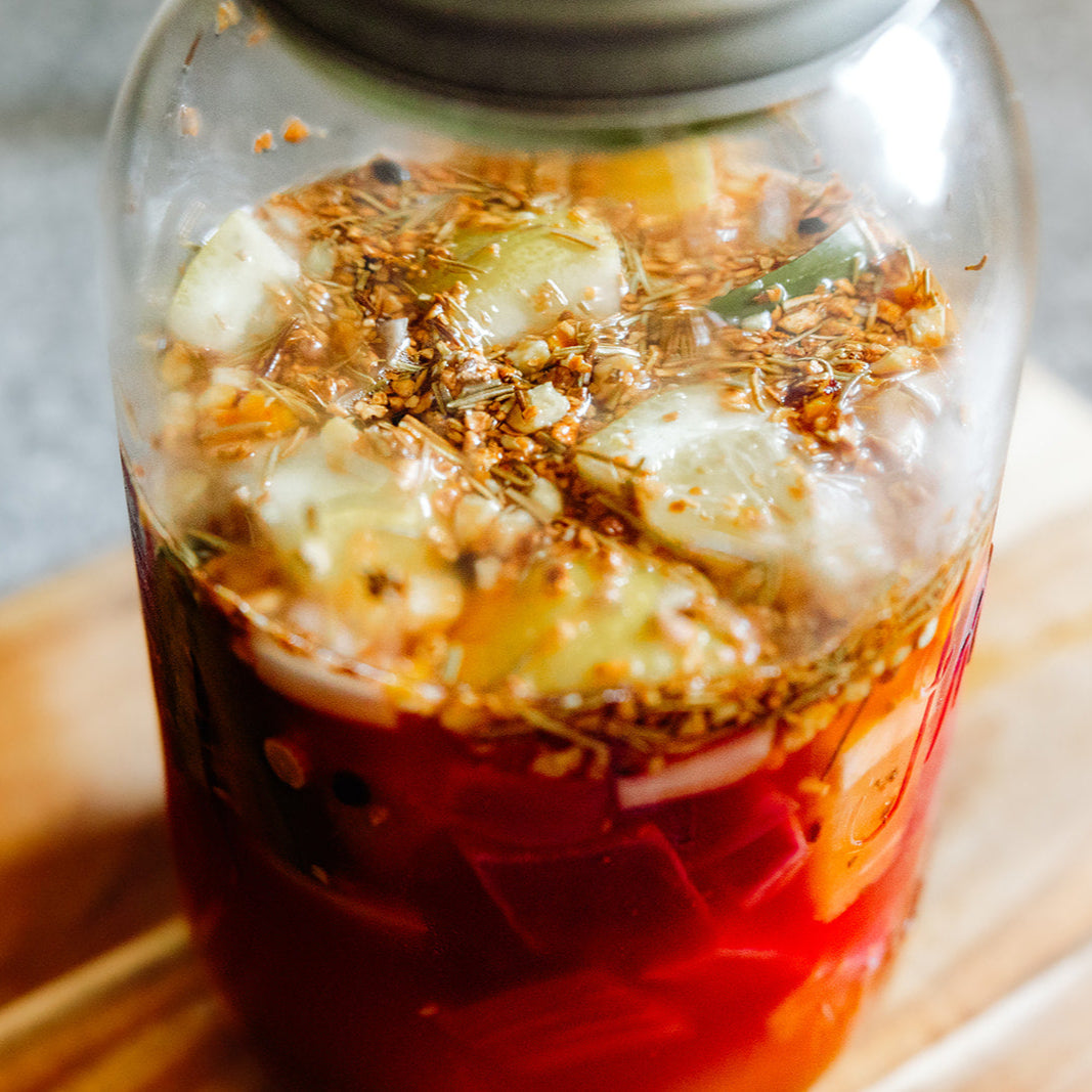Glass jar with a red liquid and floating ingredients on a wooden surface