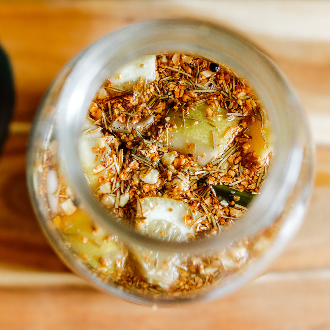 Close-up of a glass jar with a mixture of herbs and vegetables on a wooden surface.