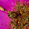 Tea leaves in a wooden scoop on a pink background