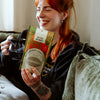 Woman holding a mug and a package of raspberry leaf tea on a couch.