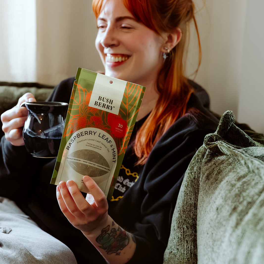 Woman holding a mug and a package of raspberry leaf tea on a couch.