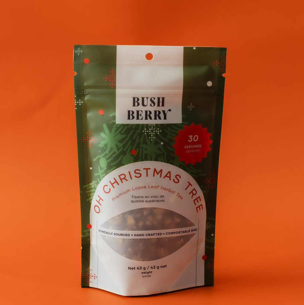 A stand-up pouch of Bush Berry 'Oh Christmas Tree' herbal tea, featuring a dark green pine tree design with a white label and red accents, set against a solid orange background.