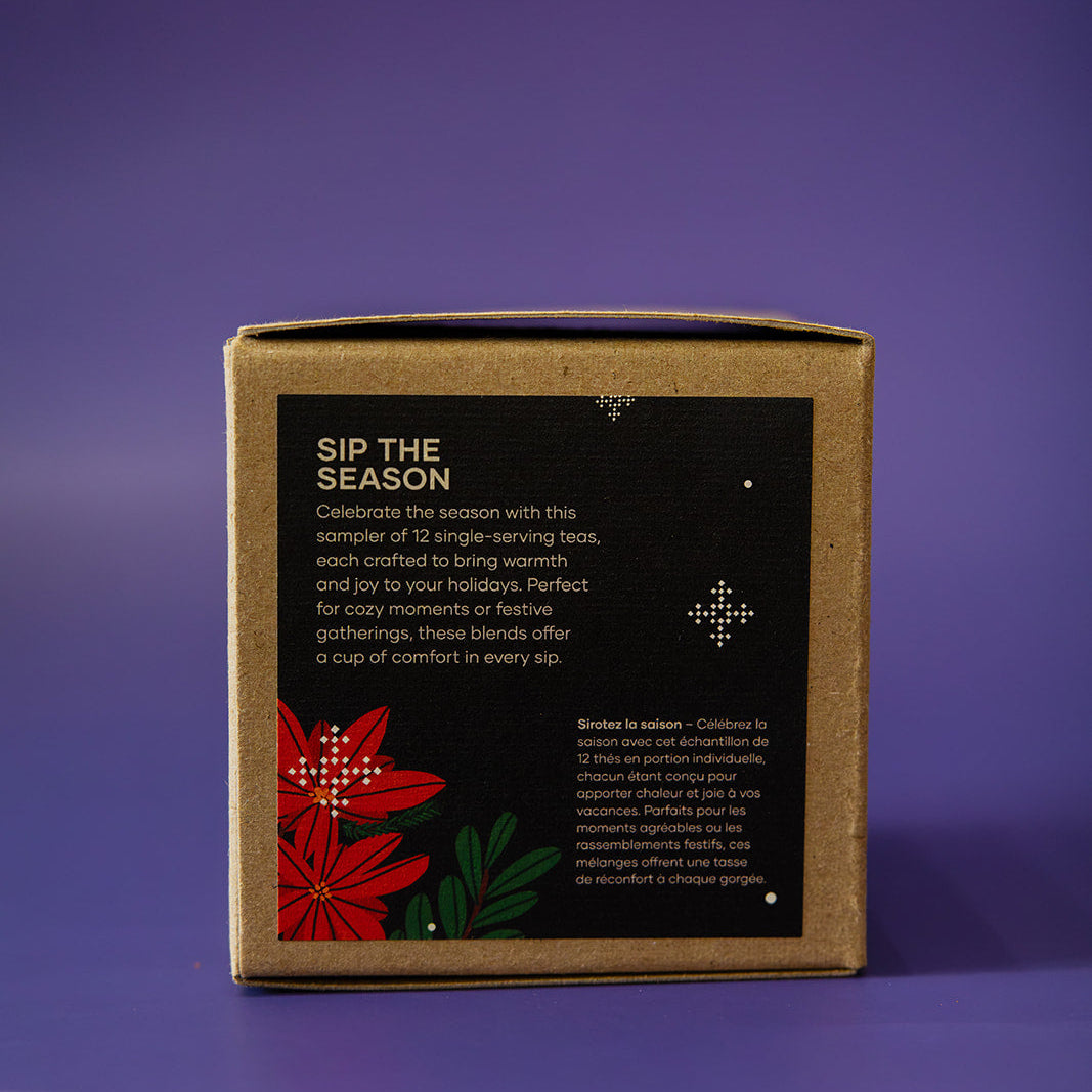 A square kraft paper box with a black label reading 'SIP THE SEASON' and decorated with red flowers and green leaves, standing on a purple background.